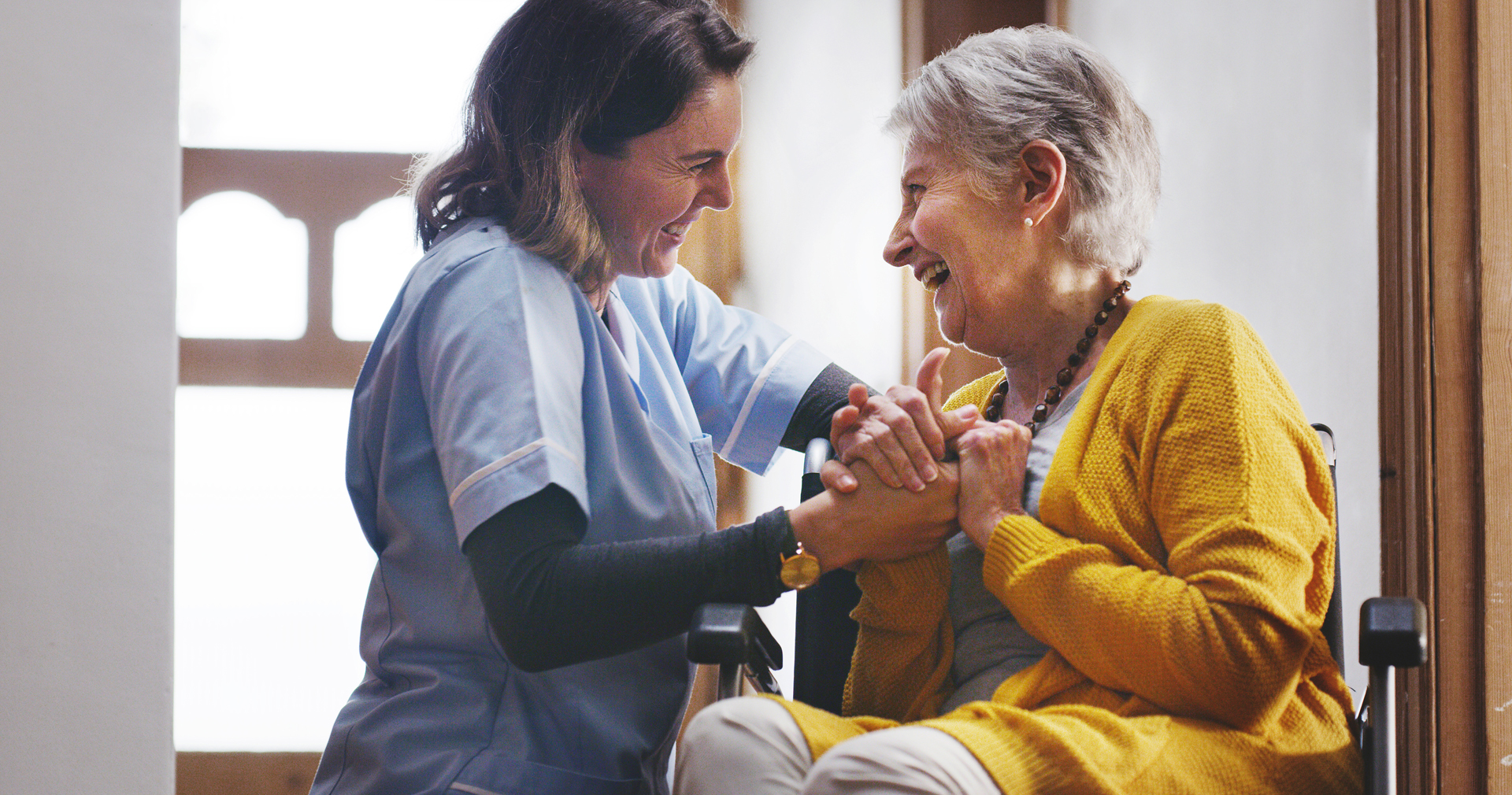 Nurse, laughing and senior woman in nursing home bonding, smiling and holding hands - health and wellness.